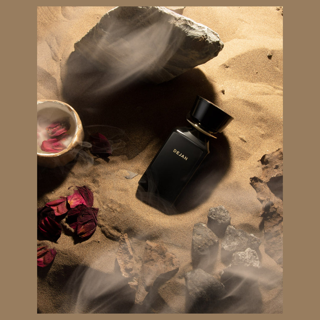 Oman Luxury Dejan Eau de Parfum bottle on desert sand with dried roses and stone