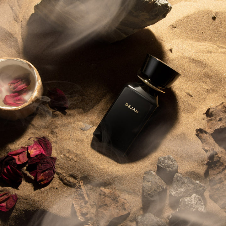 Oman Luxury Dejan Eau de Parfum bottle on desert sand with dried roses and stone